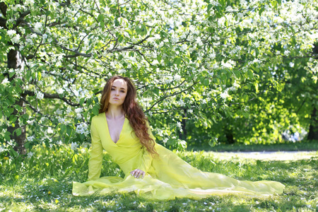女孩在黄色春天礼服反对绽放苹果树的背景