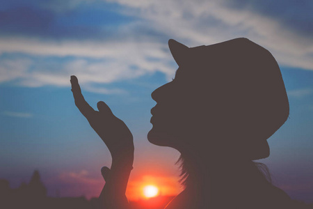 妇女在帽子送空气亲吻在日落在天空背景
