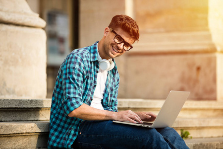 快乐的年轻学生, 戴着眼镜站在学校或大学的楼梯上, 在笔记本电脑上工作或做功课研究。