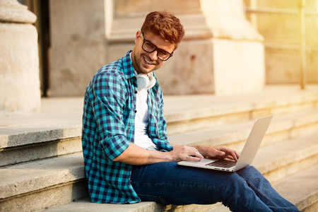 快乐的年轻学生, 戴着眼镜站在学校或大学的楼梯上, 在笔记本电脑上工作或做功课研究。