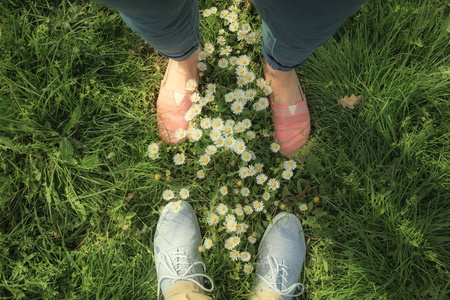 穿白色 chamomiles 的绿草甸鞋上的男女双腿