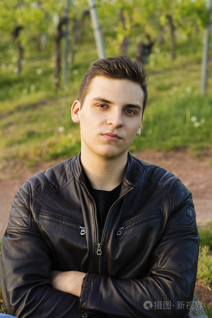 一个漂亮的年轻自信的男人穿着皮夹克坐在葡萄旁边.