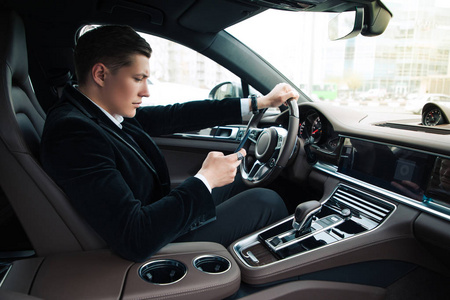 开车的时候发短信侧面视图肖像的英俊自信的年轻商人设置他的智能手机