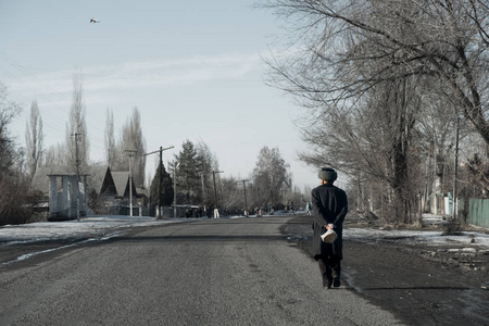 吉尔吉斯斯坦的祖父沿着小路走在村子里, 带着面包