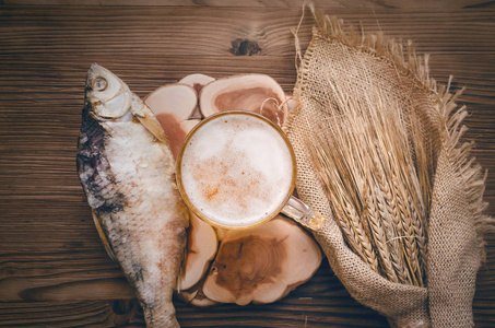 泡沫啤酒在一杯, 干鱼 stockfish 和黑麦耳朵裹在粗麻布布在烧毁的木桌背景