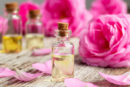 一瓶精油与新鲜的玫瑰和花瓣在木质背景
