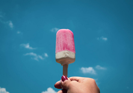 妇女手用红色钉子拿着粉红色冰冻冰棒冰弹出在夏天蓝天背景