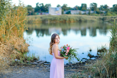 粉色话孕妇身穿粉红色连衣裙, 花花束站在湖边照片