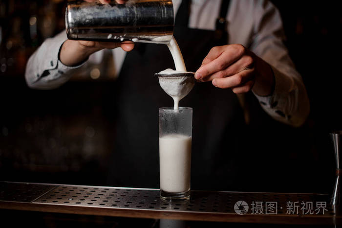 酒保把一杯酒精饮料从钢振动筛倒入饮料杯, 通过 botler 在酒吧柜台上。