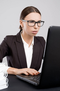 年轻细心的商业妇女坐在办公桌上的文件和书籍, 并使用笔记本电脑