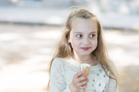 女孩甜美的牙齿上欢快的脸吃冰淇淋, 浅色的背景。手里拿着冰淇淋的小女孩。甜牙孩子与白色冰淇淋在华夫饼锥。夏日款待理念