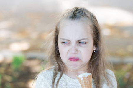 甜牙女孩与白色冰淇淋在华夫饼锥。手里拿着冰淇淋的小女孩。夏天对待概念。女孩甜牙在反感的面孔吃冰淇淋, 轻的背景