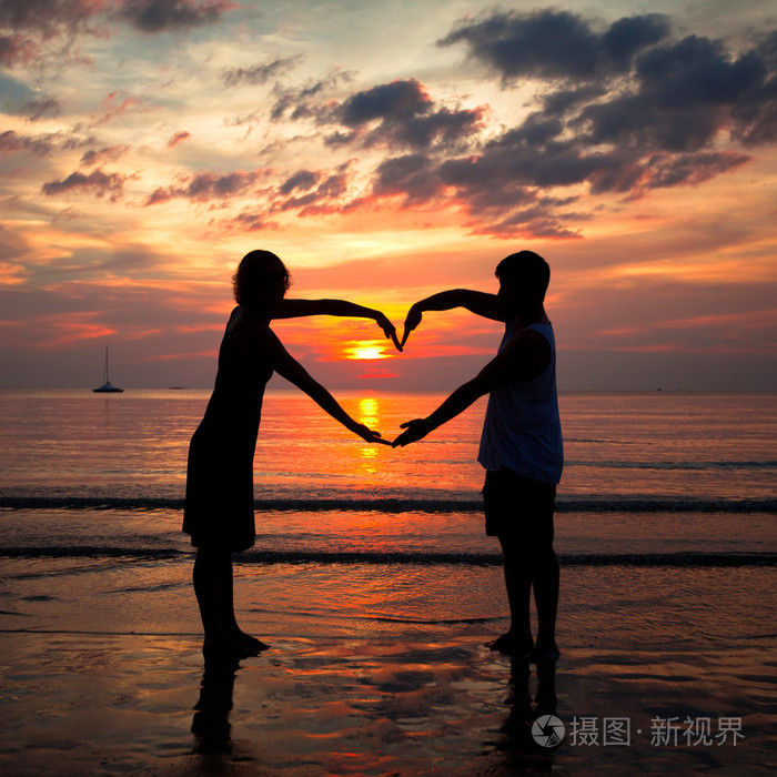 年轻夫妇心形海沙滩上在日落时手牵手