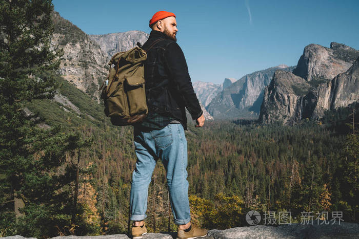时髦的家伙与背包探索野生森林土地在山上站在山顶上, 男性徒步旅行者
