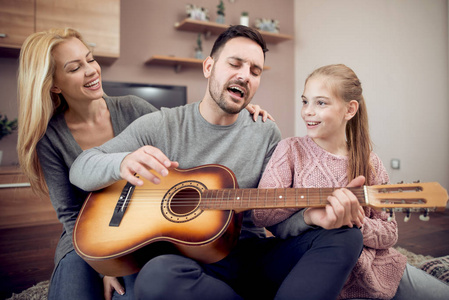 父亲教女儿玩声波吉他, 而母亲坐在地板上