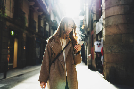 年轻的时髦女人的肖像手持手机在她的手看着在模糊的城市街道背景显示