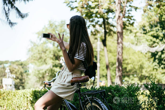 美丽的女孩坐在自行车和采取自拍与智能手机