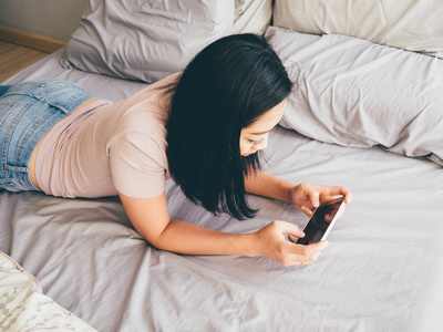 女人在她的床上玩智能手机游戏照片