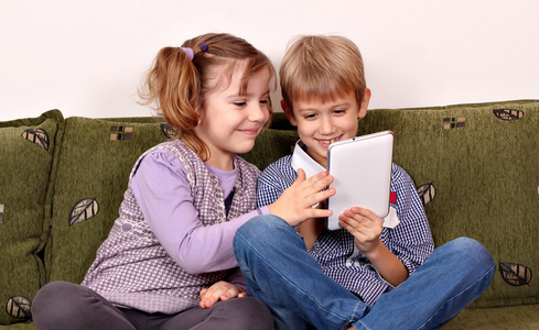 快乐的小小的女孩和男孩玩平板电脑