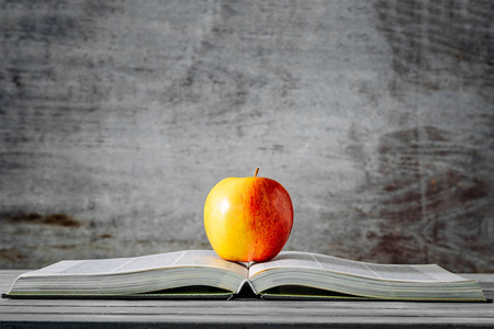 红色苹果在打开的书与木背景