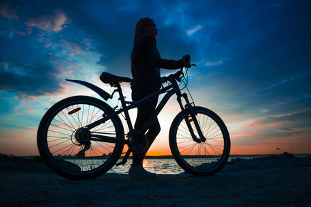 日落时带着自行车住在湖岸的年轻女子