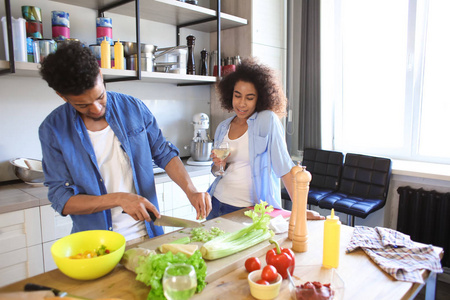 年轻的非洲裔美国妇女喝葡萄酒和她的男朋友在厨房做饭