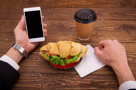 羊角面包三明治, 手提电话。咖啡在桌子上。商务午餐概念