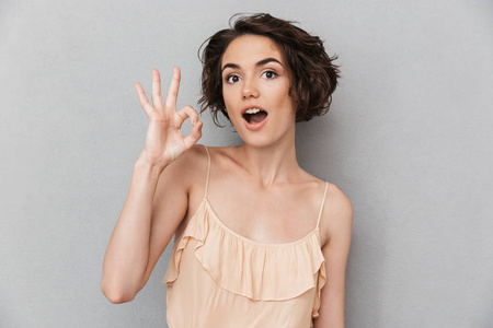 一个开朗的年轻女子的肖像显示确定的手势孤立的灰色背景
