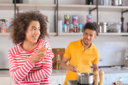 年轻的非洲裔美国妇女喝葡萄酒和她的男朋友在厨房做饭