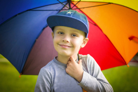 在一个阳光明媚的夏日公园里, 一个戴着五颜六色雨伞的小白男孩的肖像