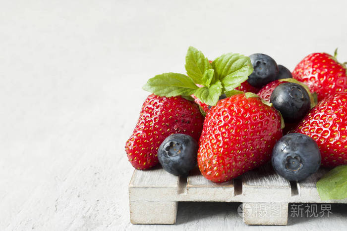 新鲜浆果草莓蓝莓薄荷在一个木制的立场, 灰色背景与复制空间文本