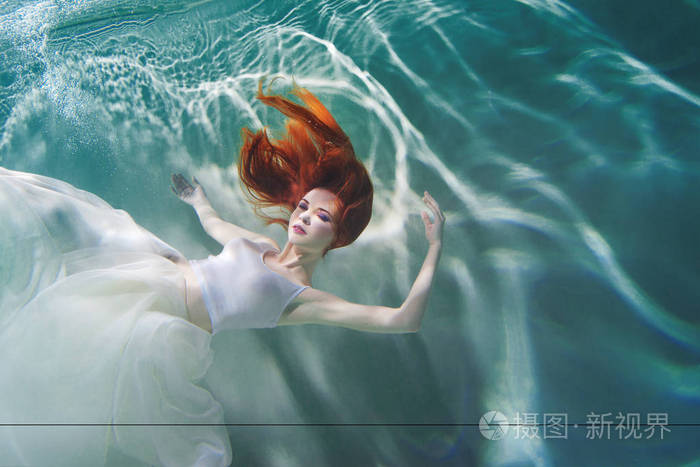 水下女孩美丽的红头发的女人穿着白色的衣服在水下游泳