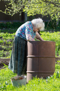 老妇人在庭院里在一个铁桶与水图片