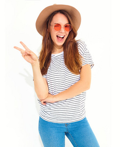 年轻时尚的笑女孩在休闲夏天的衣服, 在白色的背景下自然化妆的褐色帽子的模型。眨眼显示和平标志