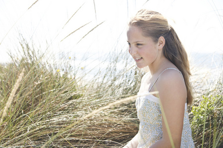 女孩坐下来与海滩上，长长的草微笑