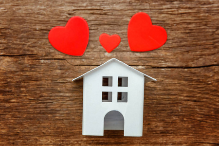 迷你白色玩具房子与三红心在一个质朴的老式木制背景。按揭财产保险梦之家概念