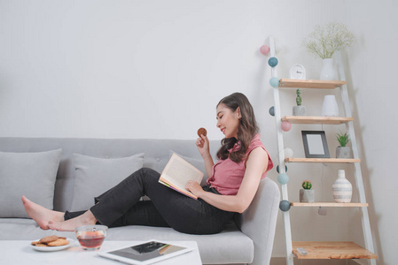 快乐的年轻女人读故事书坐在沙发上在家