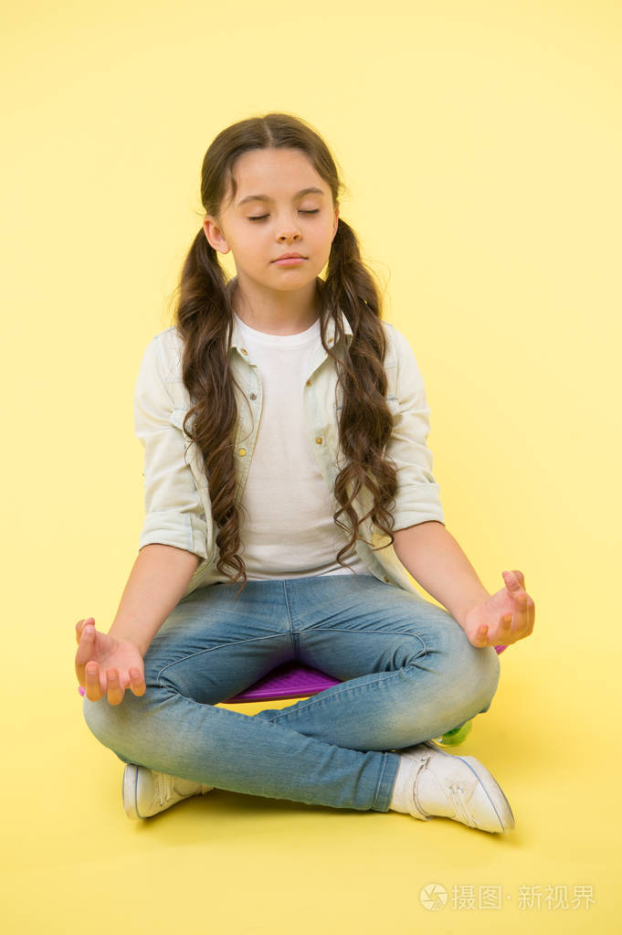 小女孩沉思坐在钱板上的黄色背景.瑜伽时间到了.时髦的儿童活动.