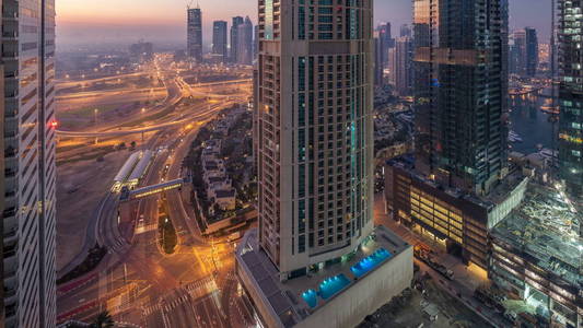 鸟瞰的一个路口和现代塔楼在一个大城市的夜到天过渡 timelapse。阿联酋迪拜滨海区城市景观与汽车和摩天大楼