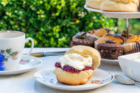 下午茶与蛋糕和传统的英语烤饼与草莓果酱和凝结奶油设置在一个桌子上的花园。户外餐饮