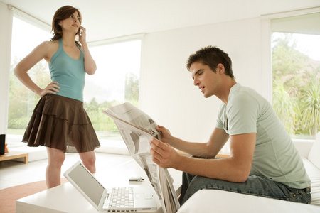 年轻夫妇在家中，使用一台笔记本电脑和打了电话