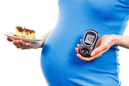 孕妇拿着一块蛋糕，在妊娠期间的糖尿病的概念与结果测量血糖水平的血糖仪期待新生儿