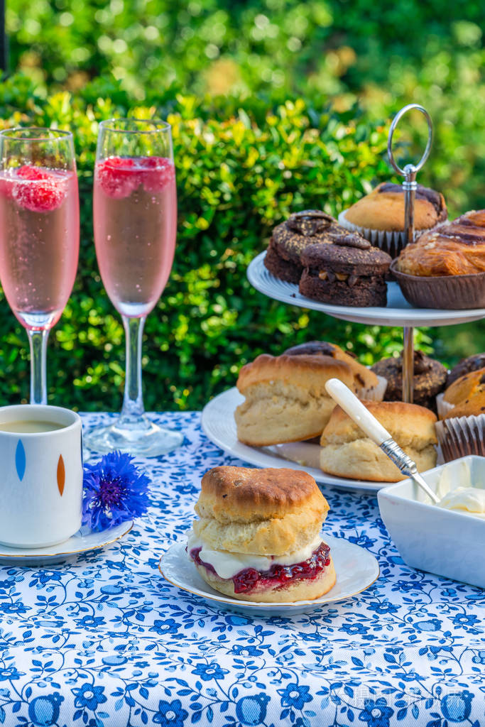 下午茶与蛋糕和传统的英语烤饼与草莓果酱和凝结奶油设置在一个桌子上