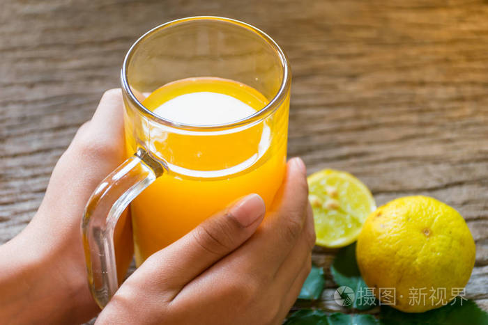 手捧着一杯橙汁喝在老木桌上每天早上新鲜的早餐橙色放在玻璃边饮用高