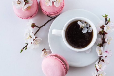 粉红色的杏仁与一杯咖啡和一枝白色的花朵在白色的背景。法式甜点和花盛开的樱桃。樱花花粉红色玛卡龙特写
