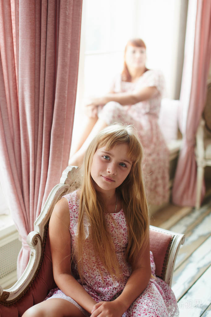 可爱的小女孩坐在沙发上, 看着相机与母亲在后台照片