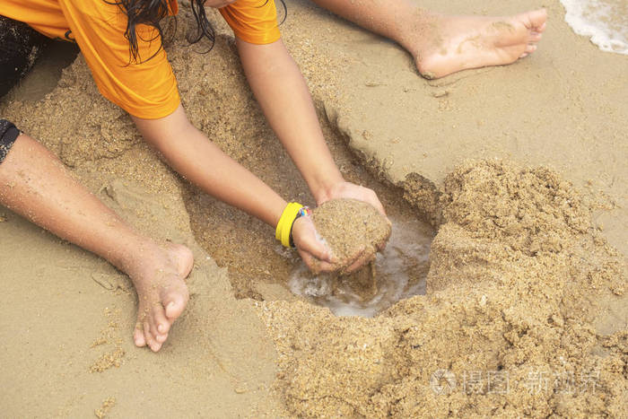 小女孩玩挖湿沙子在海滩和海浪
