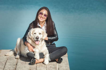 年轻漂亮的女人坐在码头与她的狗。户外最好的朋友