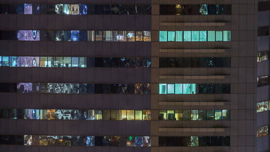 窗户的多层建筑玻璃和钢照明内和移动的人在 timelapse。在迪拜, 现代办公摩天大楼的鸟瞰图。平移左