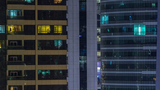 窗户的多层建筑玻璃和钢照明内和移动的人在 timelapse。迪拜现代住宅和办公楼摩天大楼鸟瞰图